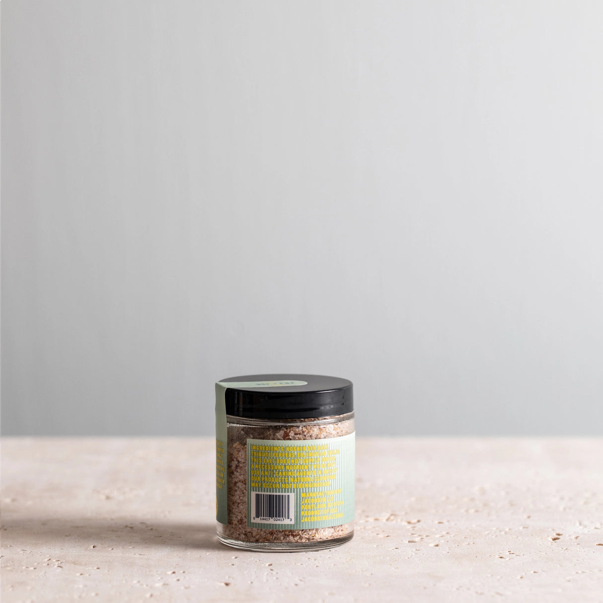 Jar of JSC x Fly By Jing Tingly Sichuan Salt with a label on a light surface and gray background