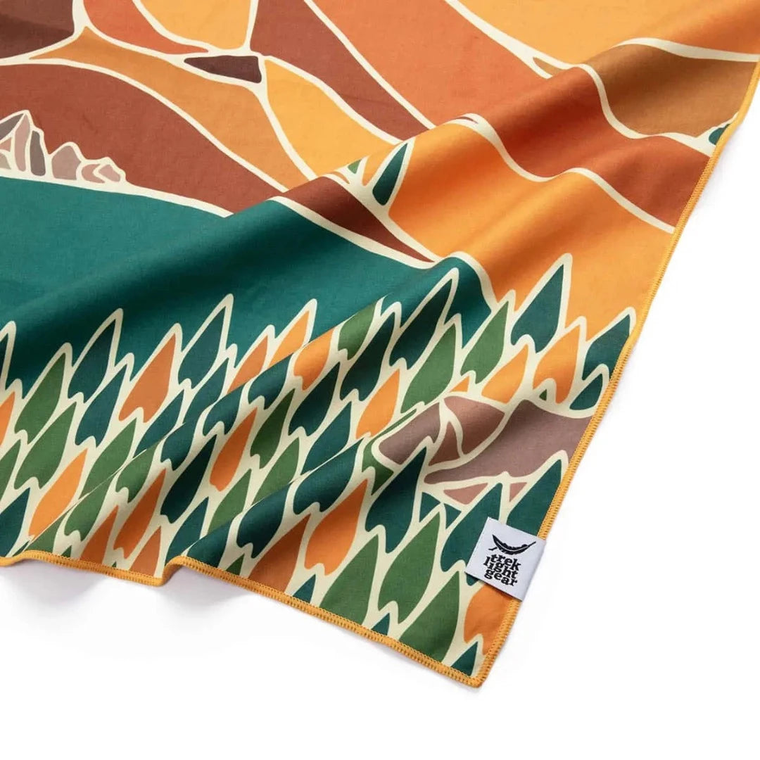 Trek Light Alpenglow Wander towel is made from recycled plastic bottles and features an abstract depiction of the mountains and sun.