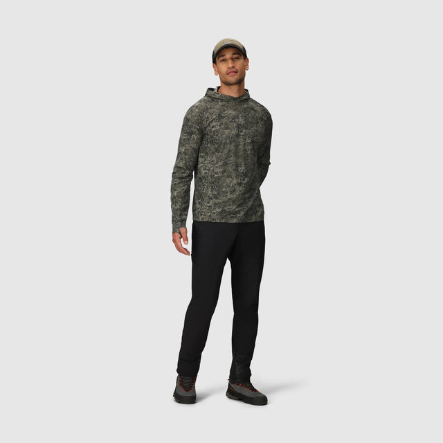 Man wearing a Outdoor Research Men's Echo Hoodie in Ranger Green Granite Print and black pants on a white background