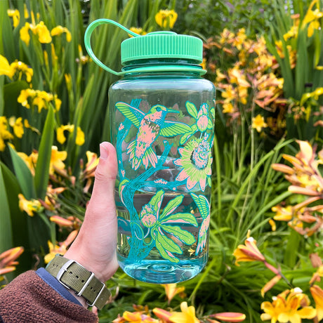 Hand holding a colorful Mustard Beetle Hummingbirds, 32oz Nalgene Water Bottle with floral design against a garden background