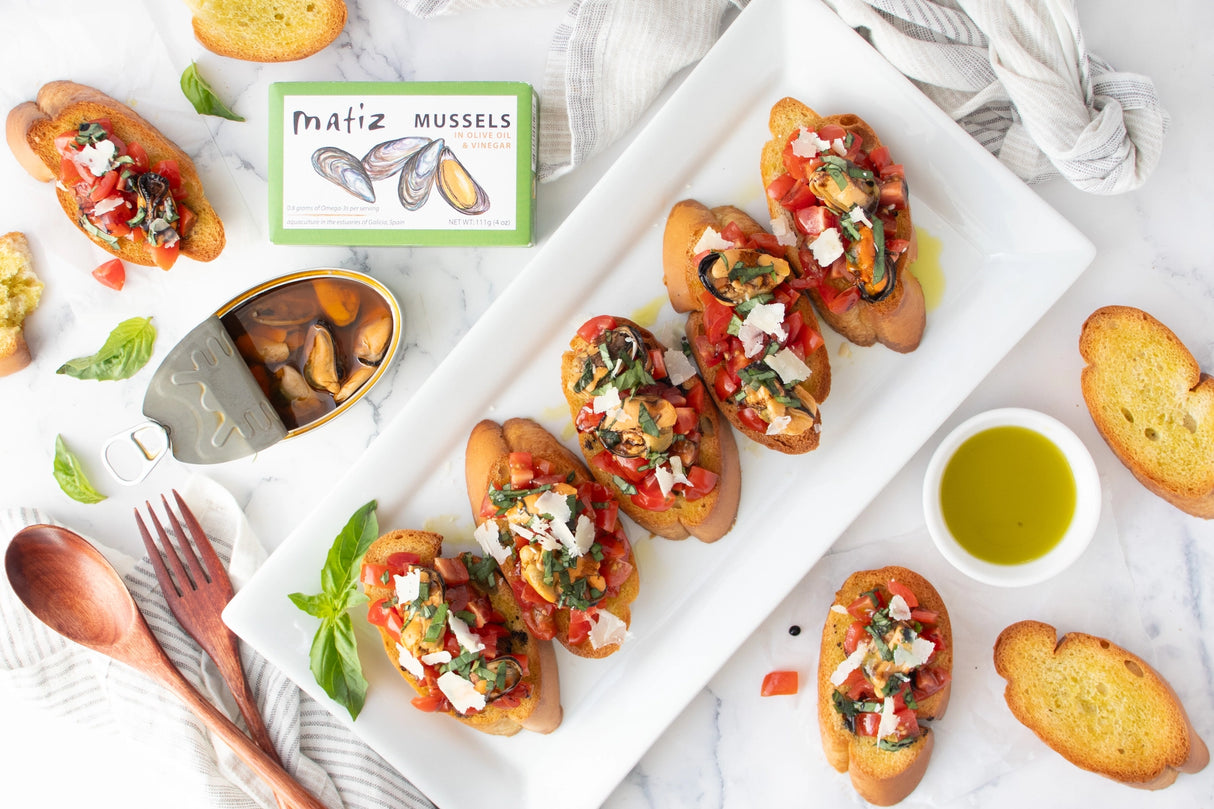 Platter of bruschetta with Matiz Mussels in Olive Oil & Vinegar packaging on a marble surface