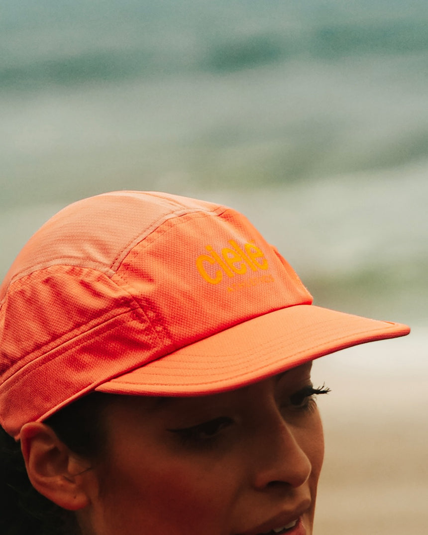 Person wearing a Ciele Athletics GOCap Classic - Athletics Blossom Coral running cap against a blurred natural background