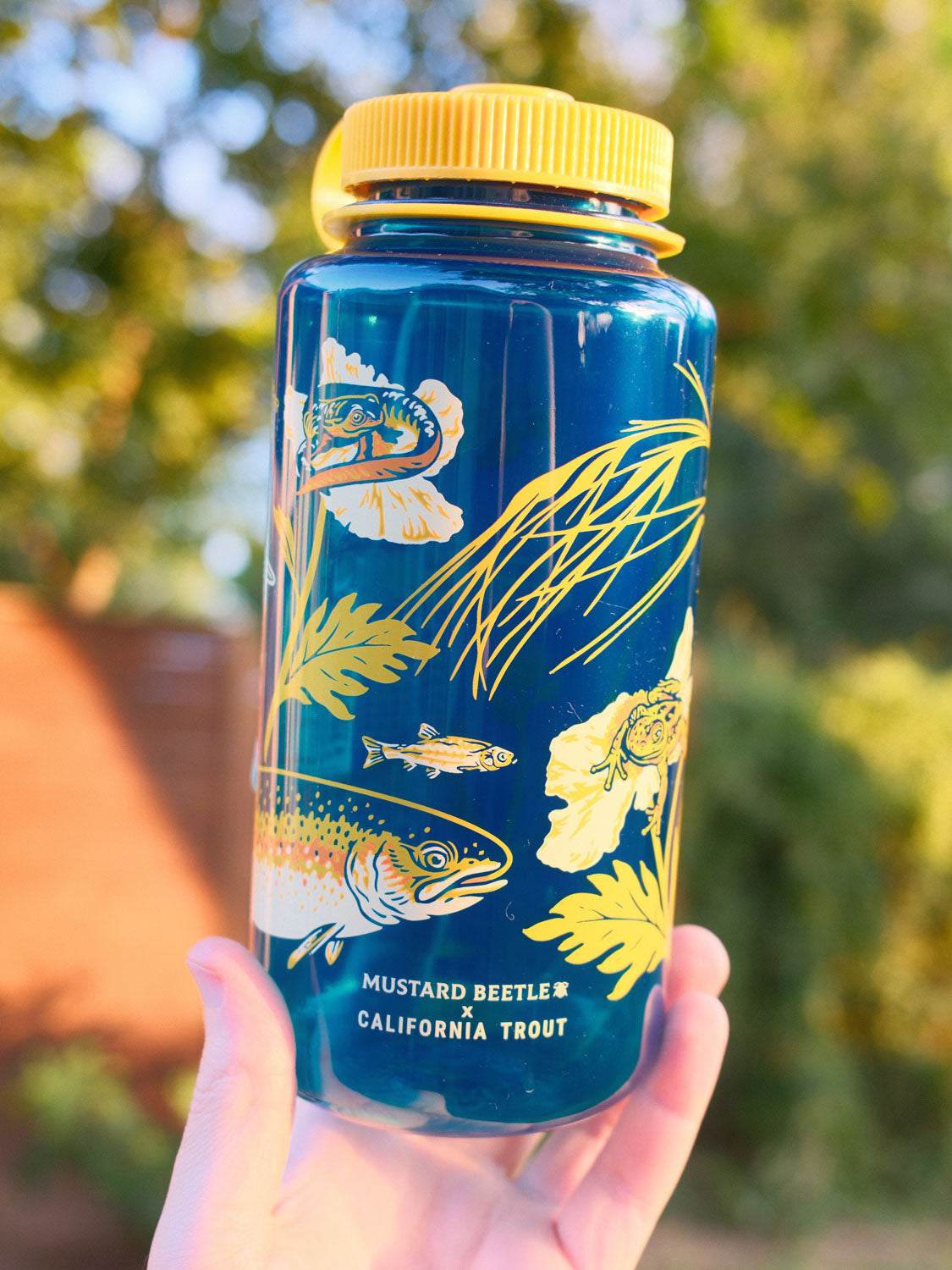 Malibu Creek for CalTrout blue Nalgene water bottle with yellow lid and nature-themed design held in front of a blurred natural background