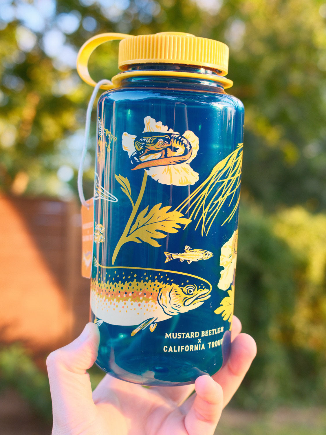 Malibu Creek for CalTrout blue Nalgene water bottle with yellow lid and nature-themed design held in a hand outdoors.
