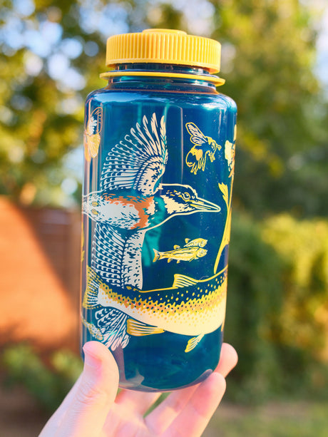 Malibu Creek for CalTrout blue Nalgene water bottle with yellow cap and nature-themed design held in front of a blurred natural background
