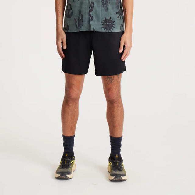 Person wearing Roark Serrano 7" Active Stretch Shorts in Black and a patterned shirt on a white background