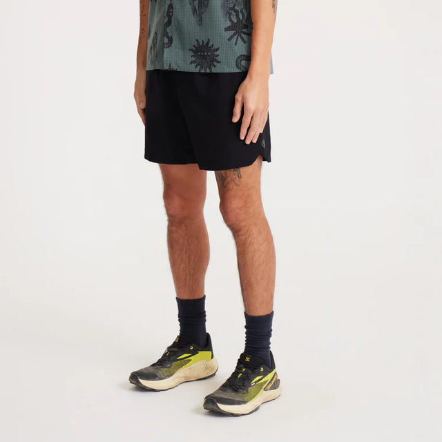 Person wearing Roark Serrano 7" Active Stretch Shorts in Black and black sneakers on a white background