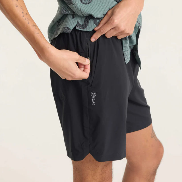 Person wearing Roark Serrano 7" Active Stretch Shorts in Black with a brand logo on a light background