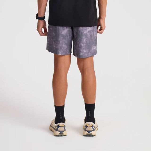 Person wearing black t-shirt, Roark Serrano 7" Active Stretch Shorts in Shark, and white sneakers on a light gray background