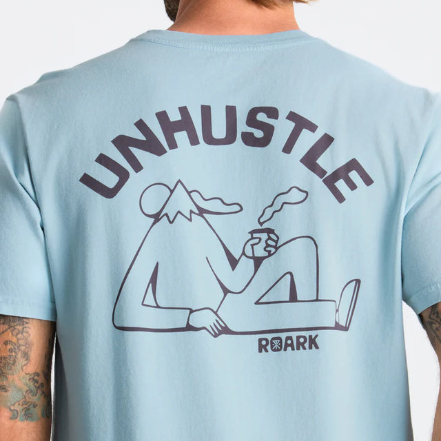 Light blue Roark Unhustle Premium Tee with 'UNHUSTLE' graphic and 'Roark' branding on a plain background