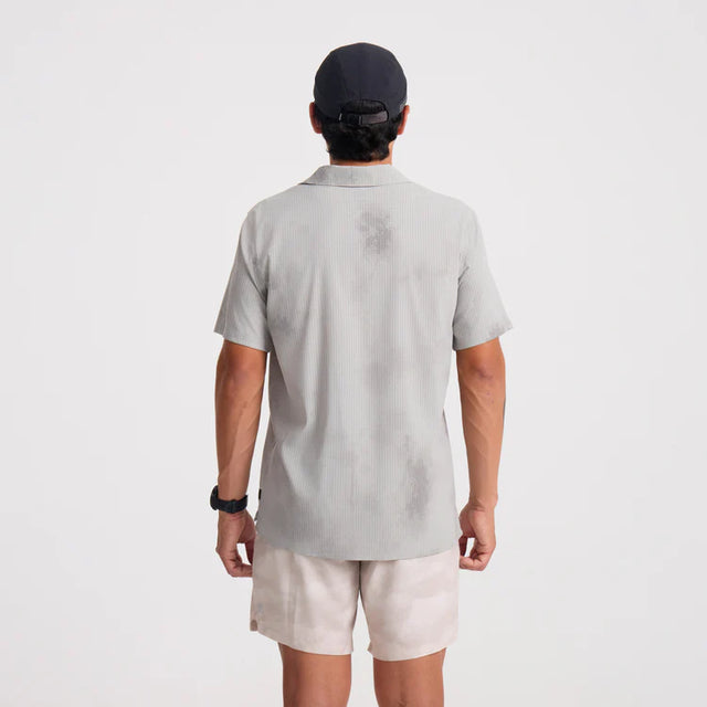 Person wearing a Roark Bless Up Trail Button Up Shirt in Ghost Grey and beige shorts on a white background