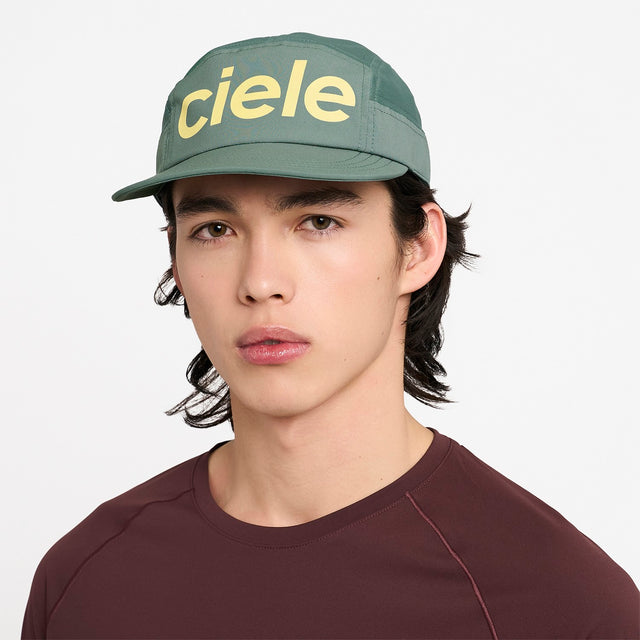 Person wearing a Ciele Athletics GOCap Comp Century Silver Pine green running cap with 'ciele' branding on a white background