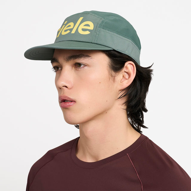 Person wearing a Ciele Athletics GOCap Comp Century Silver Pine green running cap with 'Ciele' logo on a white background