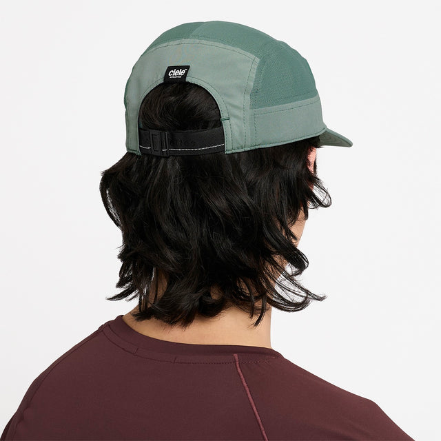 Person wearing a Ciele Athletics GOCap Comp Century Silver Pine green running cap on a white background