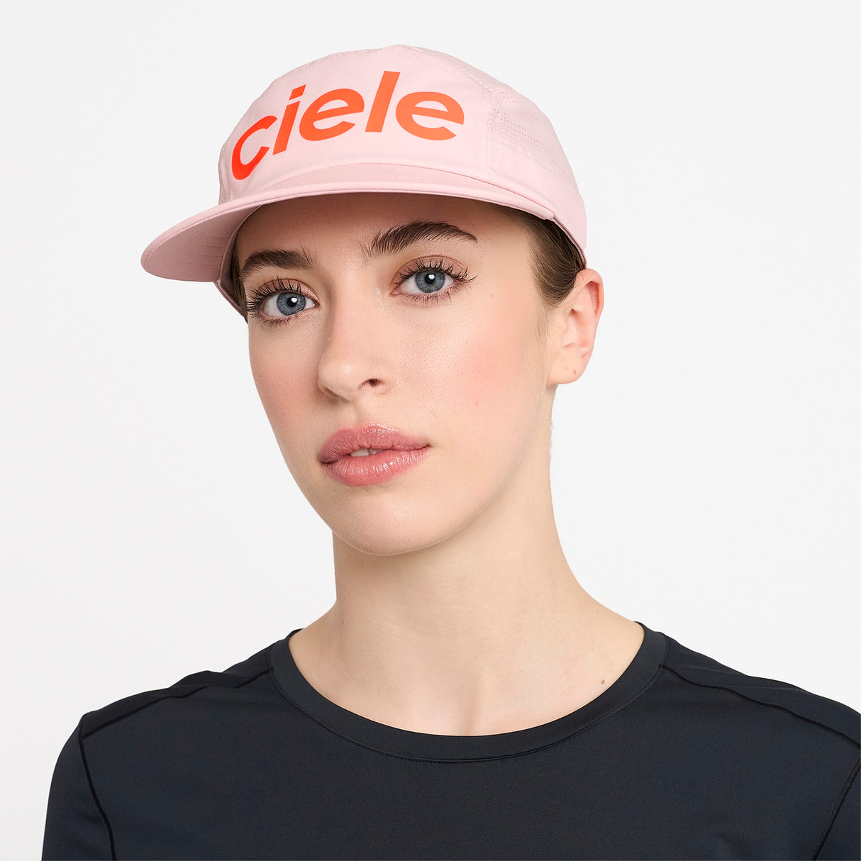 Person wearing a Ciele Athletics GOCap Comp Century Peachskin pink running cap with 'ciele' branding on a white background