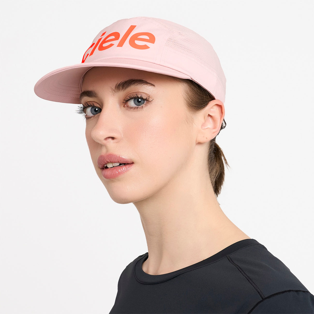 Woman wearing a Ciele Athletics GOCap Comp Century Peachskin pink running cap with 'Ciele' logo on a white background