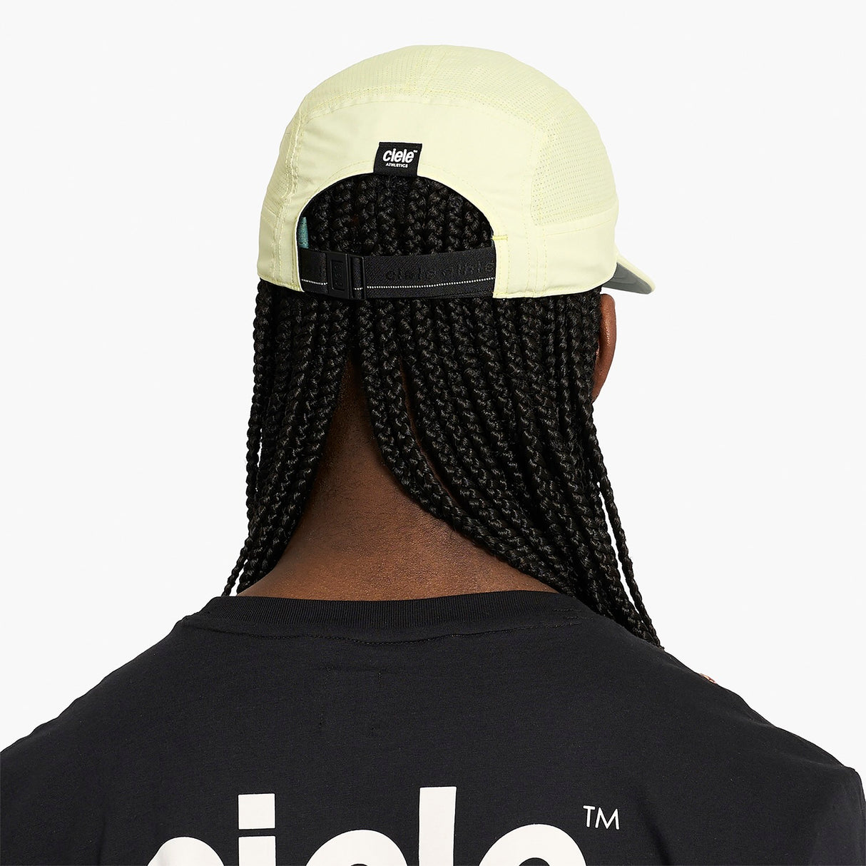 Person wearing a ciele athletics GOCap Comp - Bars Glade light yellow running cap with visible brand logo on a white background