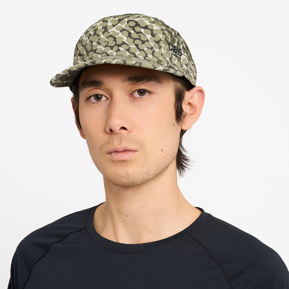 Person wearing a Ciele Athetlics GOCap SC Field - All Over Dotra running hat in Canvas with a brand logo on a white background