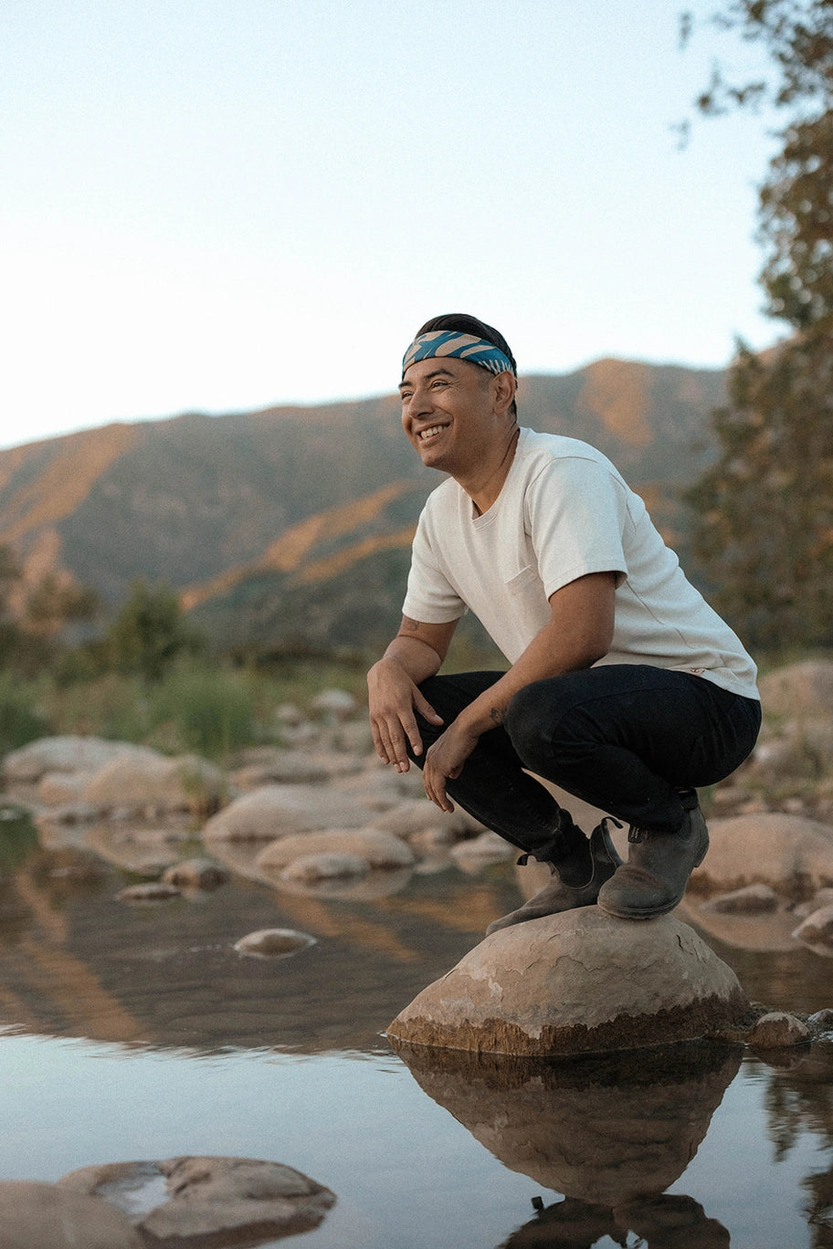Man sitting on a rock by a water body with Bandits El Rito Nights Bandana