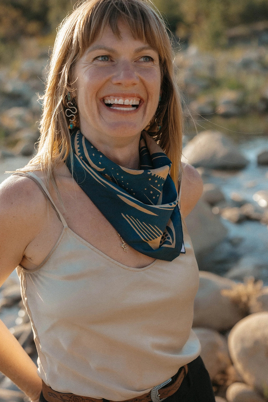 Woman wearing a Bandits El Rito Nights Bandana with a nature design, standing by a river.