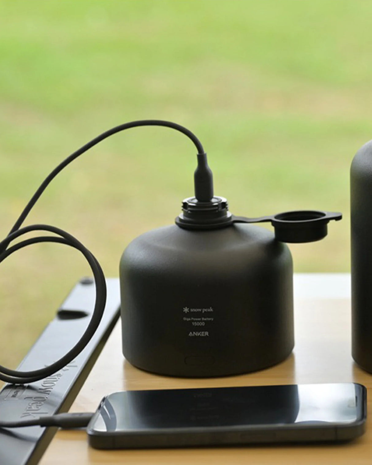Snow Peak GigaPower Battery USB camp charger charging a phone outdoors.