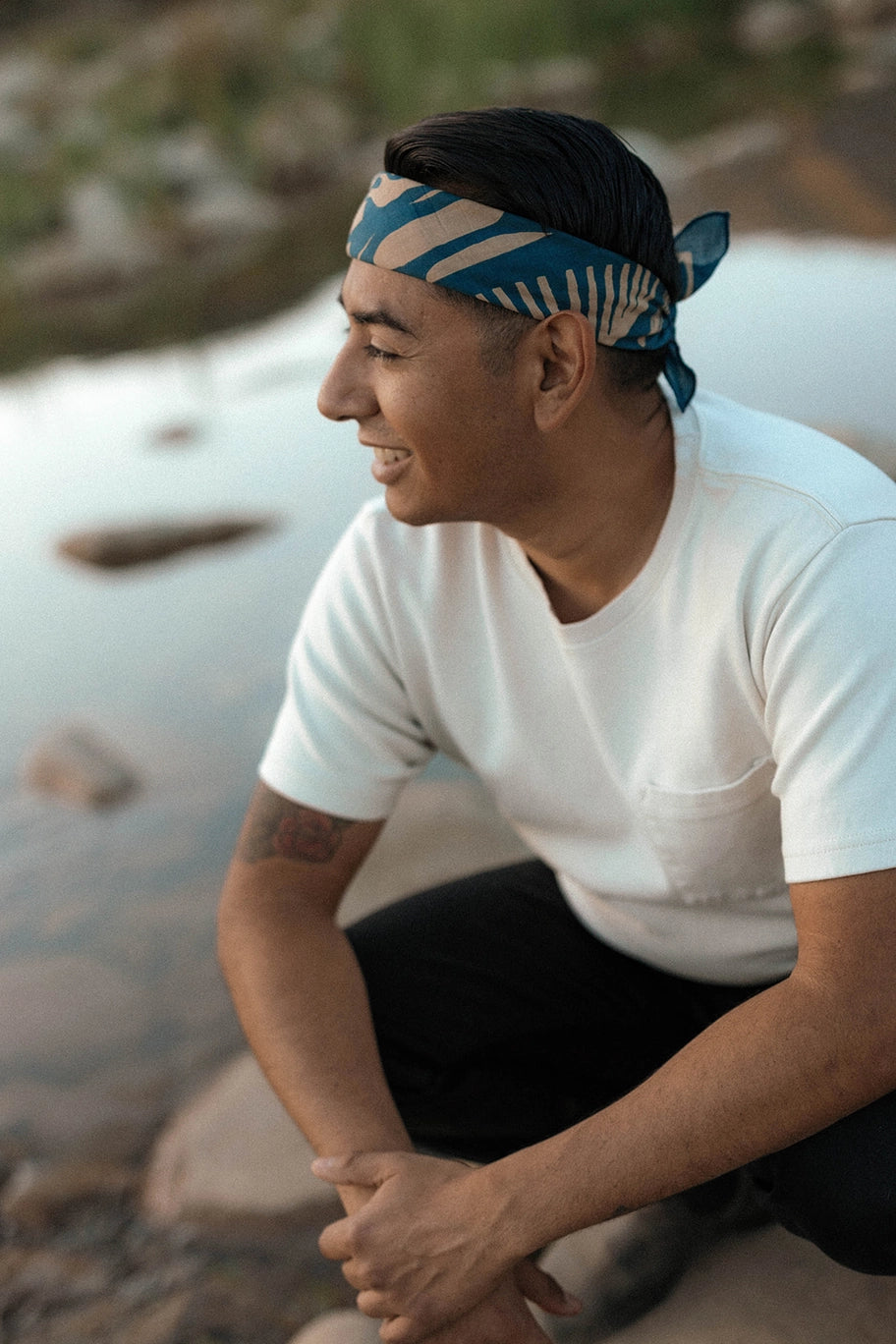 Man sitting by a body of water wearing a white t-shirt and a Bandits El Rito Nights Bandana.