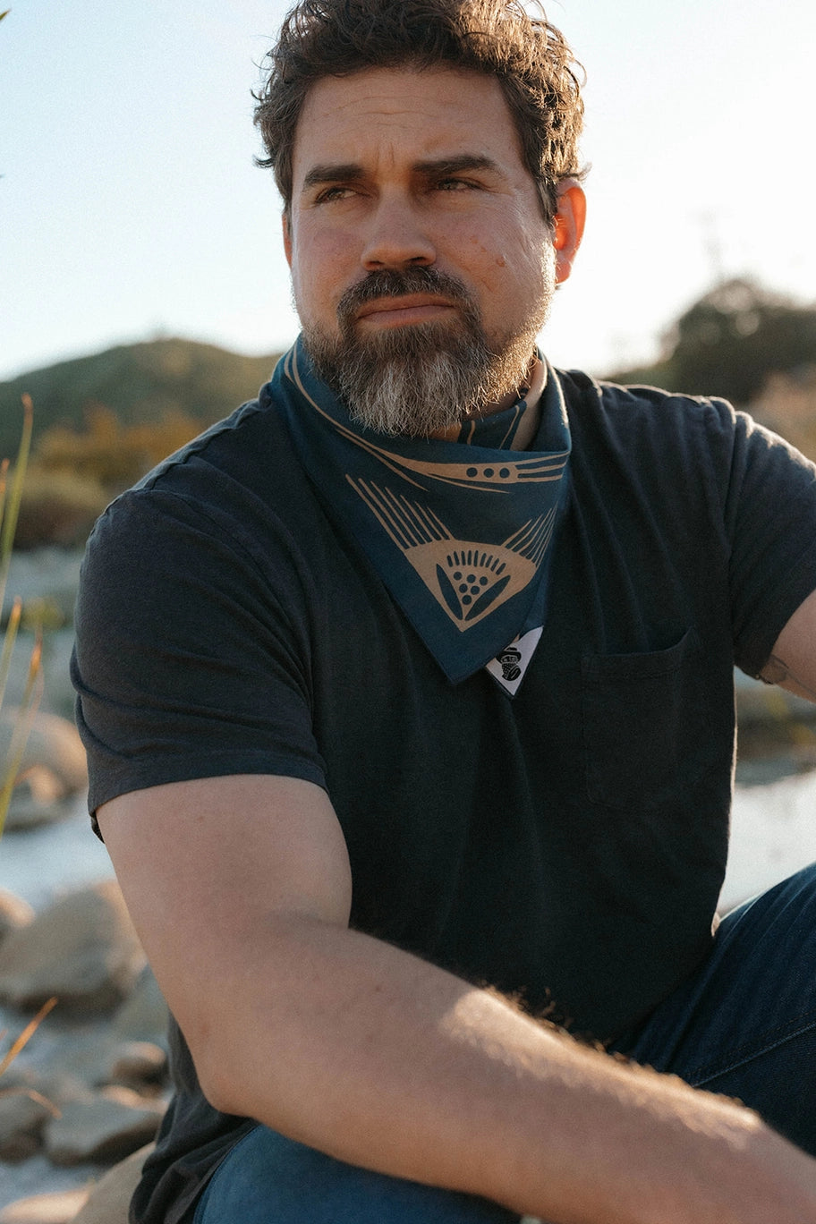 Man sitting on a beach wearing a Bandits El Rito Nights Bandana