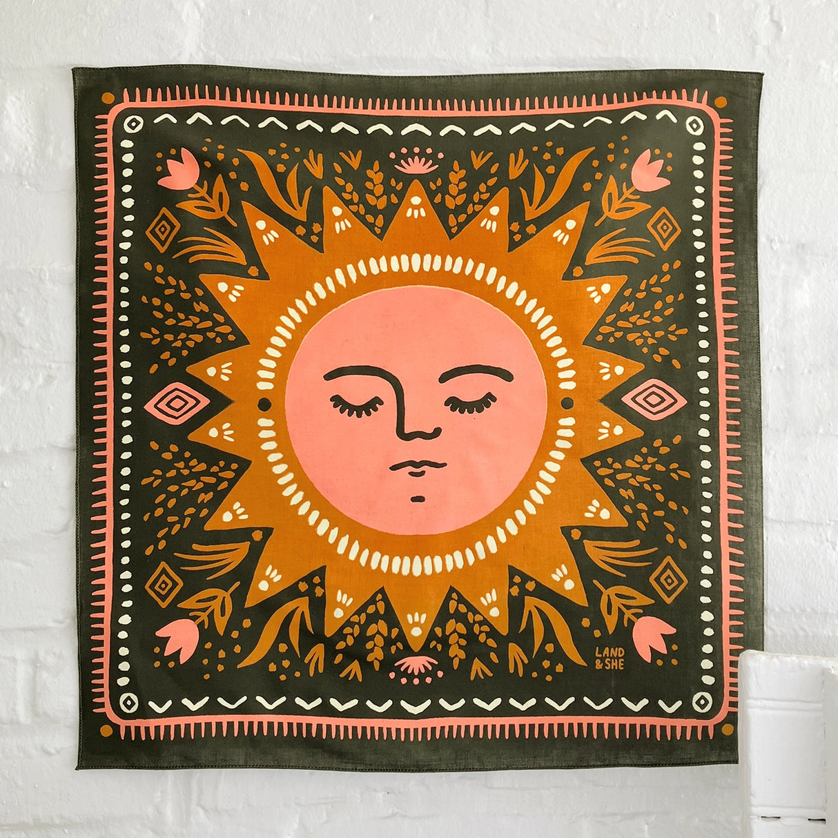 Land & She Sun Still Rises Bandana on a neutral brick background.