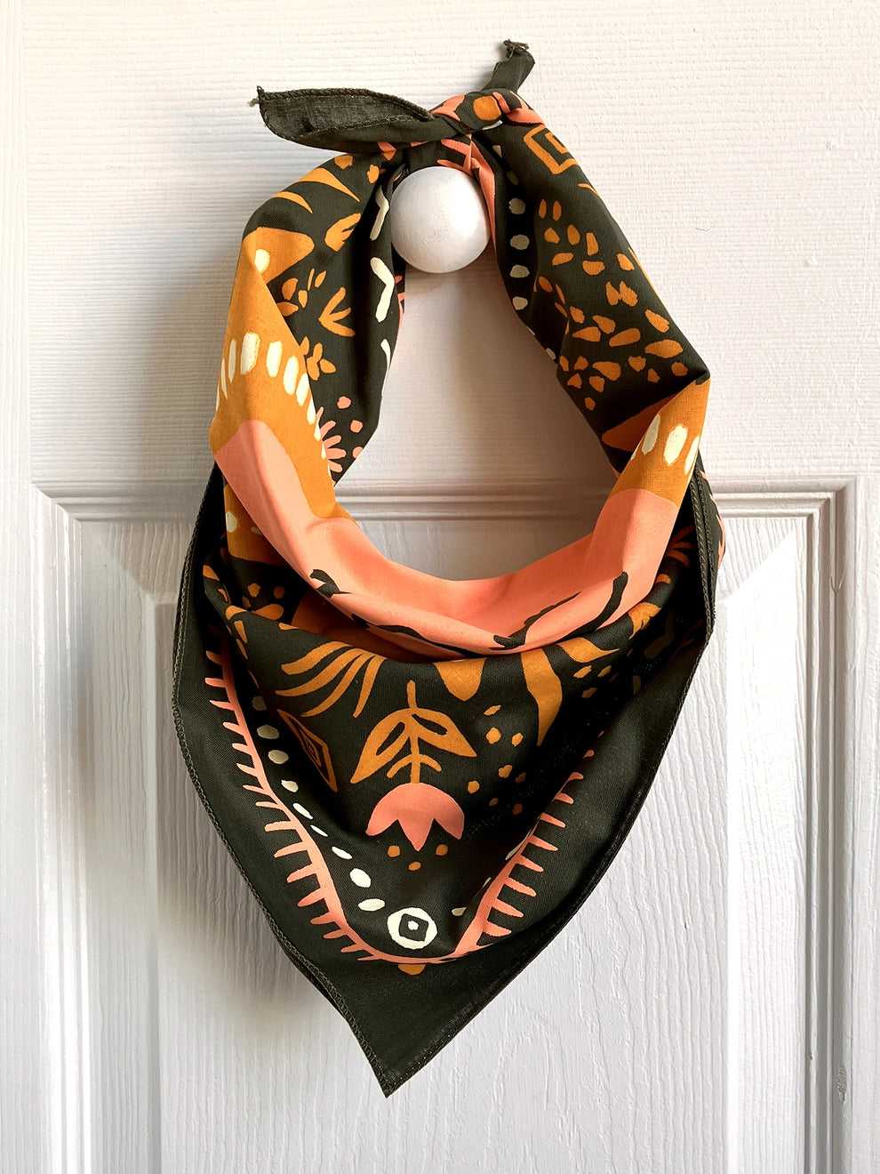 Land & She Sun Still Rises Bandana tied and hung around a hat rack.