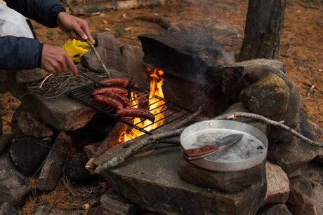 Sausages being cooked over a campfire.