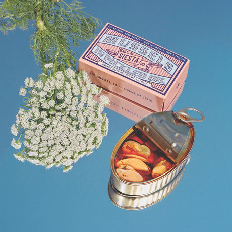 Siesta Co. Mussels in Organic Pickled Oil with pickled mussels, white flowers, and a box on a blue background