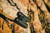 Nocs Provisions Pro Issue 8X Waterproof Binoculars in Alpine Green on a rocky outcrop.