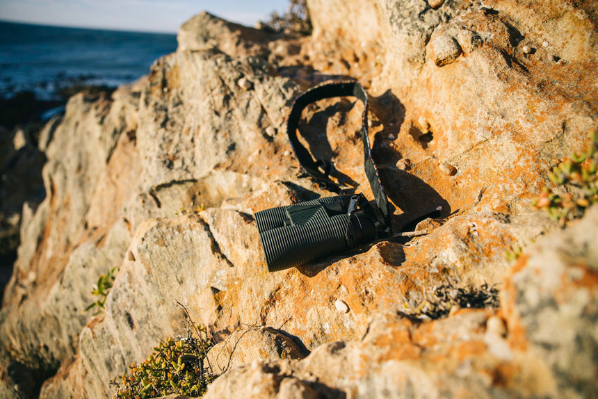 Nocs Provisions Pro Issue 8X Waterproof Binoculars in Alpine Green on a rocky ocean outcrop.