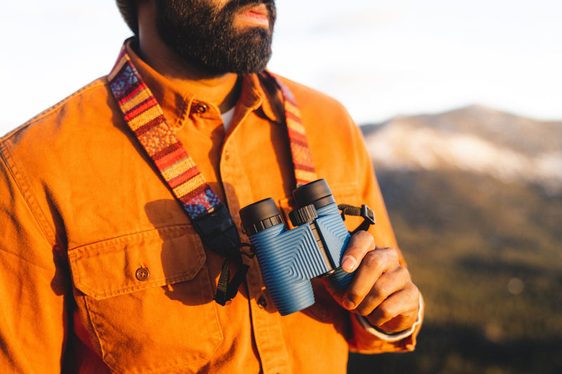 Nocs Standard Issue 10x25 Waterproof Binoculars being worn around the neck outdoors.