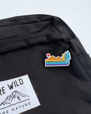 Keep Nature Wild Retro Pride pin features a mountain and forest design in the colors of the Pride flag.