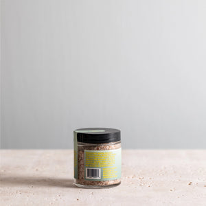 Jar of JSC x Fly By Jing Tingly Sichuan Salt with a label on a light surface and gray background
