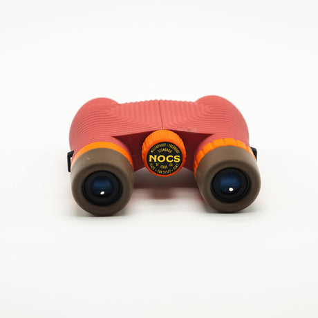 Nocs Standard Issue 10x25 Waterproof Binoculars in manzanita red on a neutral background and showing the eye pieces.