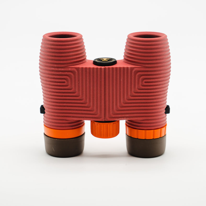 Nocs Standard Issue 10x25 Waterproof Binoculars in manzanita red from above on a neutral background.