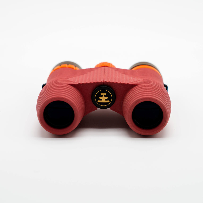 Nocs Standard Issue 10x25 Waterproof Binoculars in manzanita red showing the lenses on a neutral background.