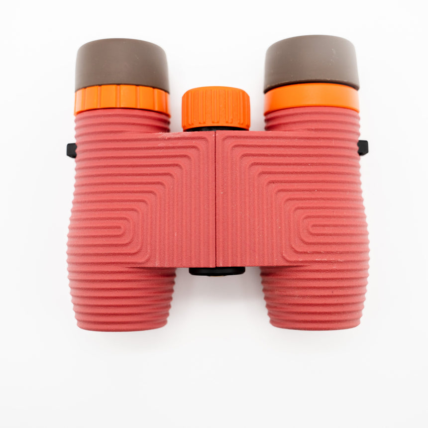 Nocs Standard Issue 10x25 Waterproof Binoculars in manzanita red from above on a neutral background.