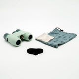 Nocs Standard Issue 8x25 Waterproof Binoculars in glacial blue on a neutral background showing the pouch and strap it comes with.