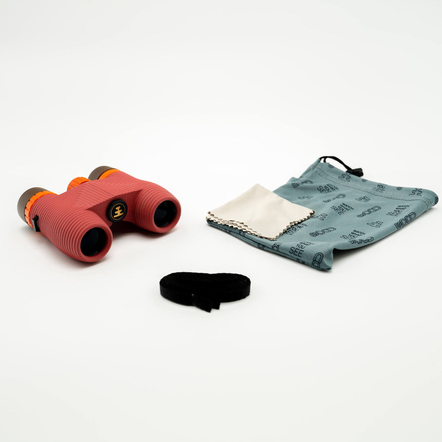 Nocs Standard Issue 10x25 Waterproof Binoculars in manzanita red showing the pouch and strap it comes with on a neutral background.