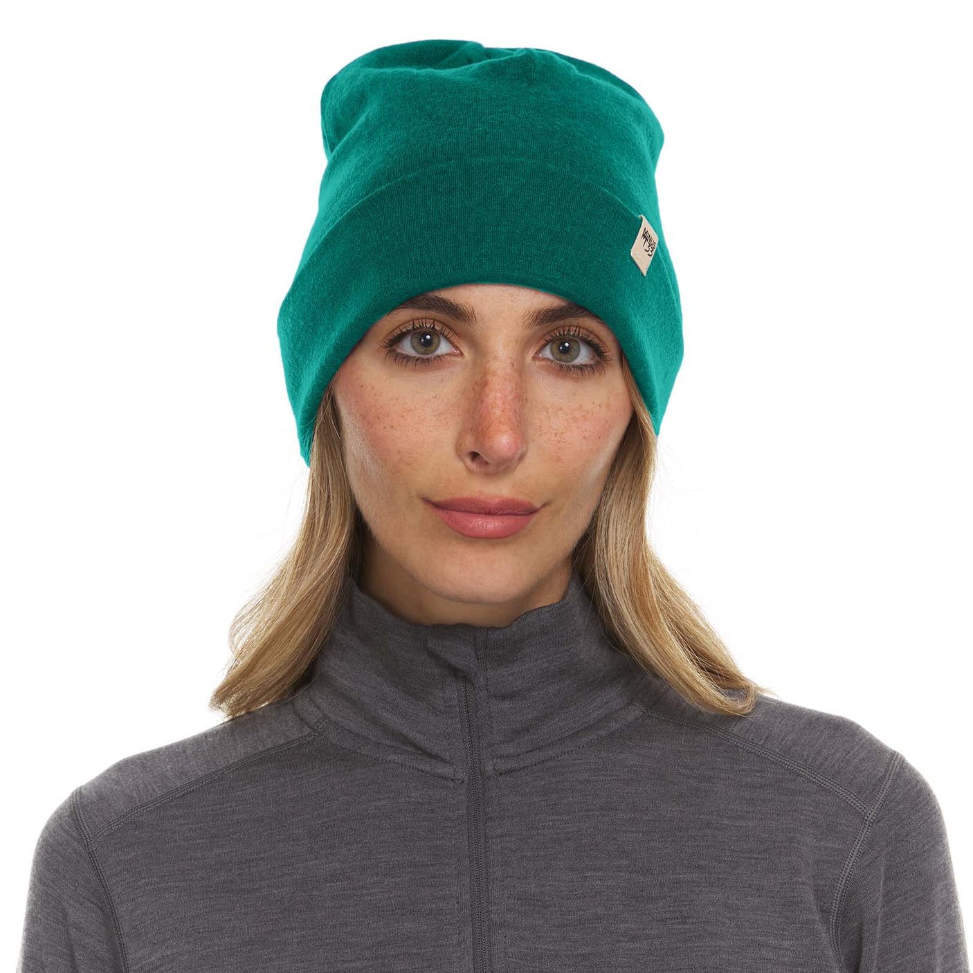 Minus33 Ridge Cuff Merino Wool Beanie in Emerald Green being worn by a woman on a neutral background.