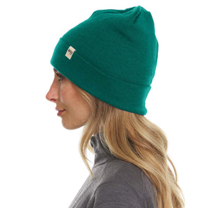 Minus33 Ridge Cuff Merino Wool Beanie in Emerald Green being worn by a woman on a neutral background.