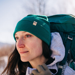 Minus33 Ridge Cuff Merino Wool Beanie in Emerald Green being worn by a woman by a woman outdoors.