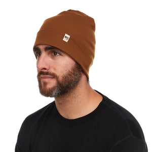 Minus33 Ridge Cuff Merino Wool Beanie in Golden Brown being worn by a man on a neutral background.