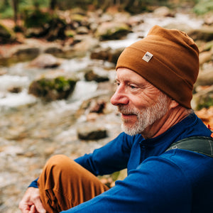 Minus33 Ridge Cuff Merino Wool Beanie in Golden Brown being worn by a man outdoors.