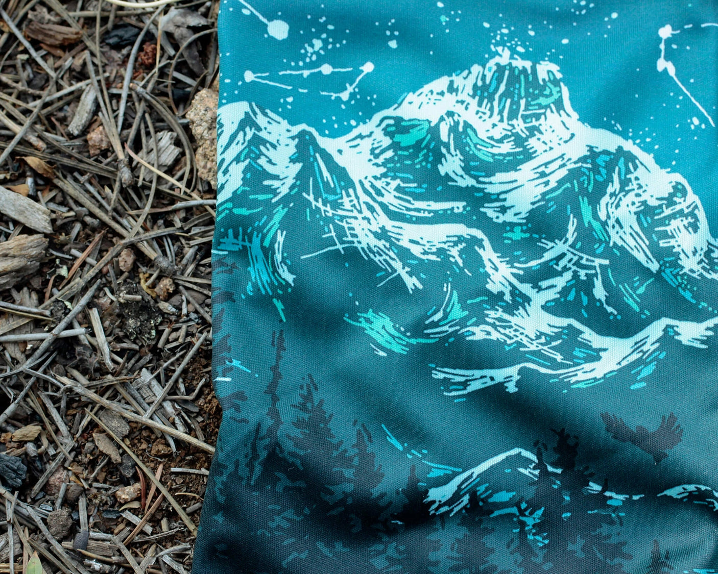 Closeup of Alpinecho's Stargazer Neck Gaiter in Turquoise on a forest floor.