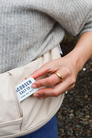 Person holding a beige jacket with a Jacobsen Salt Co. Kosher Sea Salt Slide Tin.