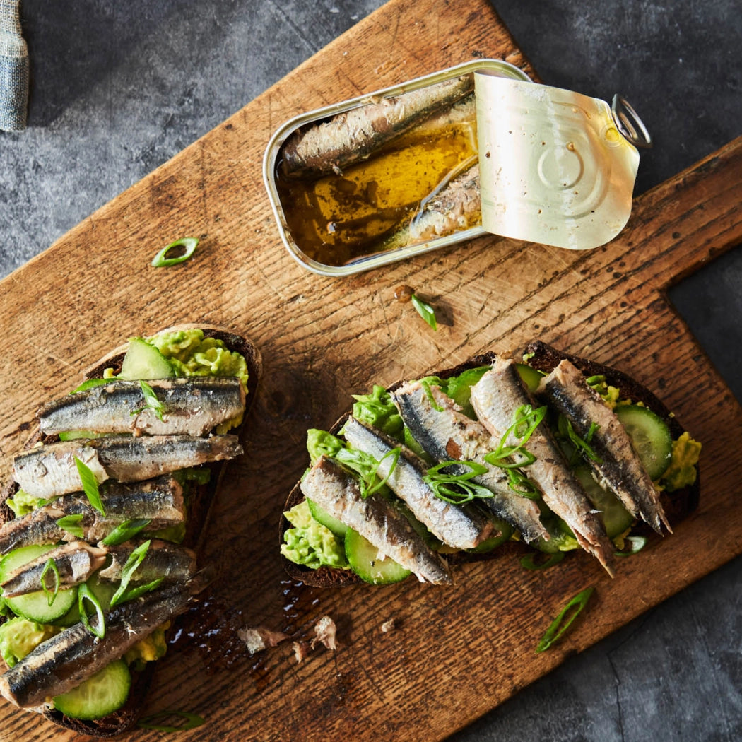 Sandwiches with anchovies and pickled vegetables on a wooden board with a can of anchovies.